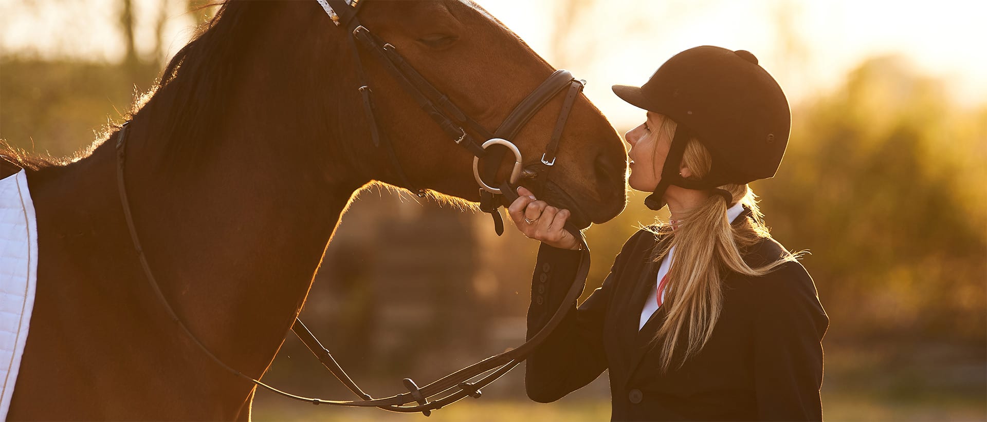 Blonde woman in riding helmet petting a brown horse's face